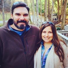 a man and woman standing next to each other on a deck in front of trees