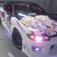 a white car with anime characters painted on it's hood and side lights, parked in a garage