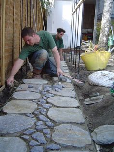 two men are working on building a house with stone walls and cobblestone walkways