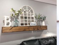 some vases and flowers are sitting on a shelf above a leather couch in a living room