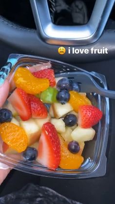 a person is holding a plastic container filled with fruit and veggies, while sitting in a car