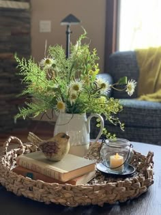 a tray with books, flowers and a candle on it sitting on a table in front of a couch