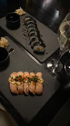 two trays with sushi and wine on the table next to eachother