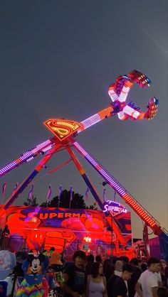 the carnival rides are brightly lit up at night with people walking around them and onlookers watching