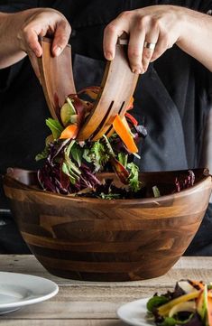 a person cutting into a salad in a wooden bowl