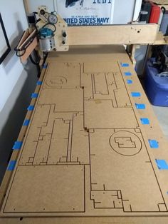 a cardboard board with blue tape on it and a machine in the background that is cut out to make a basketball court