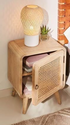 a small wooden cabinet with a light on top and a plant in the corner next to it