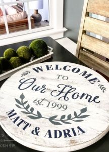 a welcome sign sitting on top of a black table next to a wooden chair and potted plant