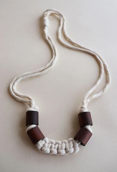 a white and brown necklace with two wooden beads hanging from it's side on a white surface