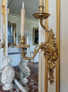 a large mirror sitting on top of a wall next to a white and gold statue