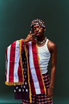 a woman in plaid shorts and a white tank top holds an american flag scarf over her face