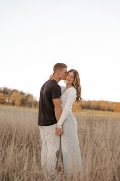 a man and woman are standing in the tall grass with their arms around each other