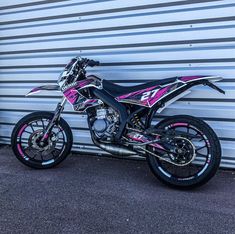 a pink and black dirt bike parked in front of a garage door with graffiti on it