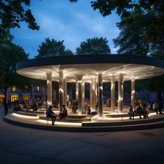 people are sitting on benches in front of a circular structure with columns lit up at night