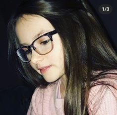 a girl with glasses looking down at her cell phone while wearing a pink sweater and black rimmed glasses