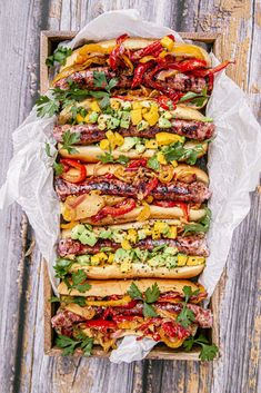 a tray filled with hot dogs covered in toppings on top of a wooden table