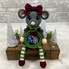 a stuffed rat sitting on top of a suitcase with a wreath around it's neck