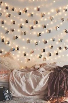 an unmade bed with pictures hanging on the wall and lights strung from above it