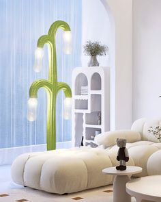 a living room filled with white furniture next to a tall green cactus plant on the wall