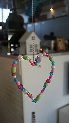 a heart shaped ornament hanging from a string with beads and other items in the shape of a house