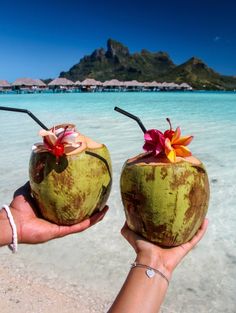 two coconuts with straws and flowers on them are held in front of the ocean