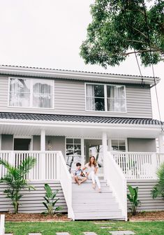 two people sitting on the steps of a house with trees and grass in front of them