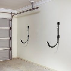 two metal hooks are attached to the wall in an empty room with white walls and gray garage doors