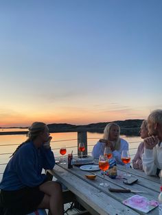 four people sitting at a table with wine glasses in front of them and the sun setting