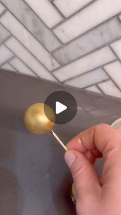 a person is holding a gold lollipop on a stick