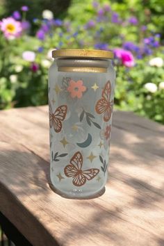 a glass jar sitting on top of a wooden table in front of flowers and butterflies