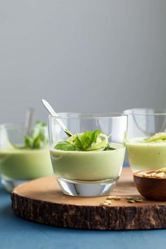 three glasses filled with green smoothie on top of a cutting board