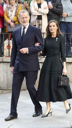 an older man and woman walking down the street in front of a group of people