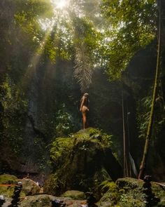 a naked woman standing on top of a rock in the middle of a lush green forest