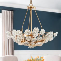 a chandelier with white flowers hanging from it's centerpiece in a dining room