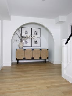 a living room with white walls and wood flooring next to a wooden dresser in front of an arched doorway