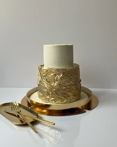 a white and gold wedding cake sitting on top of a plate next to two forks