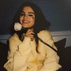 a woman sitting on a couch with a flower in her mouth and she is wearing a yellow coat