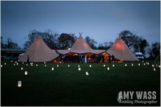 a group of people standing in front of tents with candles on the grass at night