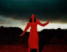 a woman in a red dress is holding her arms out and looking up at the sky