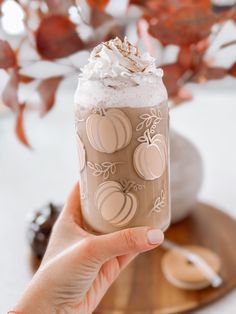 a hand holding up a drink with whipped cream and pumpkins on the top,