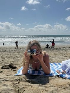 a woman laying on top of a beach under a blue and white towel holding a camera