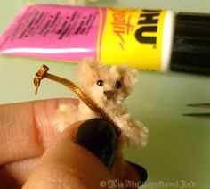 a tiny teddy bear sitting on top of a piece of wood next to a tube of glue