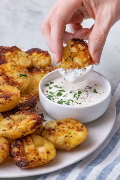 a person dipping something in a small white bowl on top of some fried potatoes with ranch dressing