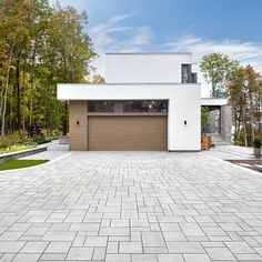 a white house with a brown garage door and brick driveway in front of the house