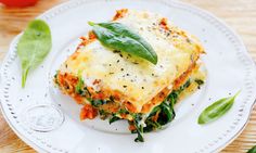 a white plate topped with lasagna covered in cheese and spinach leaf garnish