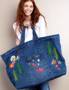 a woman is holding a large denim bag with embroidered trees and stars on the side