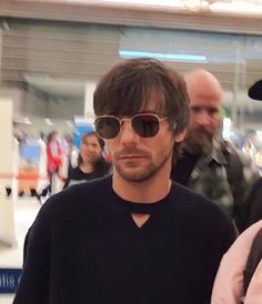 a man wearing sunglasses and a hat is standing next to another man in a black shirt