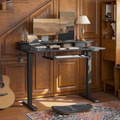 a desk with a guitar and lamp on it in front of a stair case next to a staircase