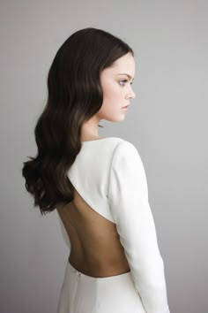 a woman with long dark hair wearing a white dress and looking off to the side