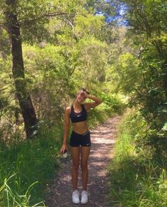 a woman standing on a dirt path in the woods with her hand to her head